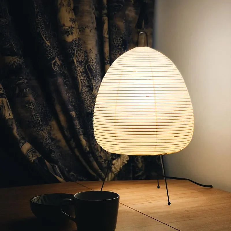 Small lamp with a textured shade on a wooden surface next to a dark curtain.
