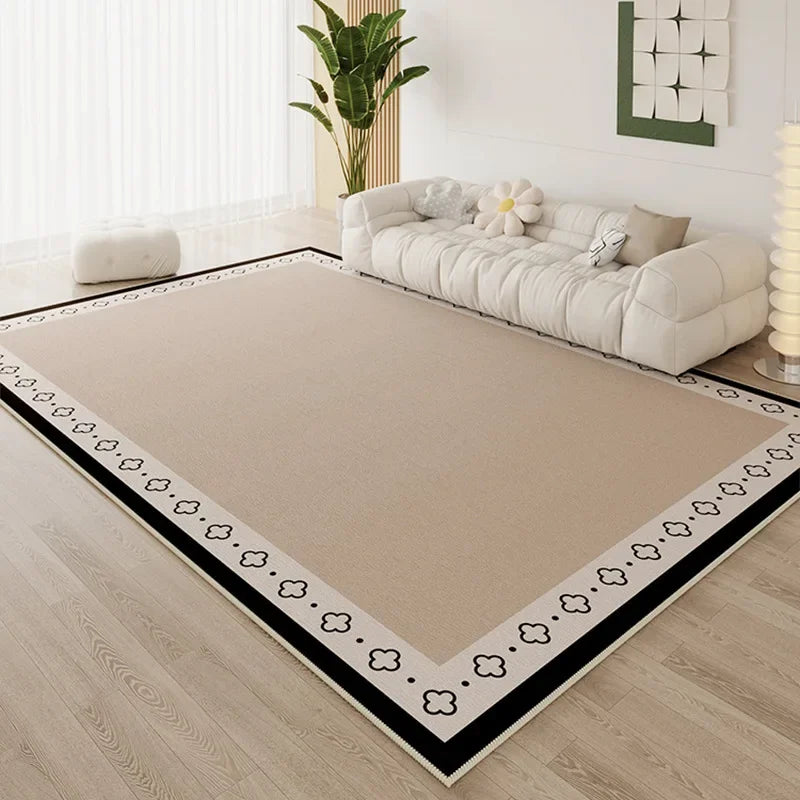 Large sand area rug with black and white clover border detail in a bright minimalist living room with white cloud sofa