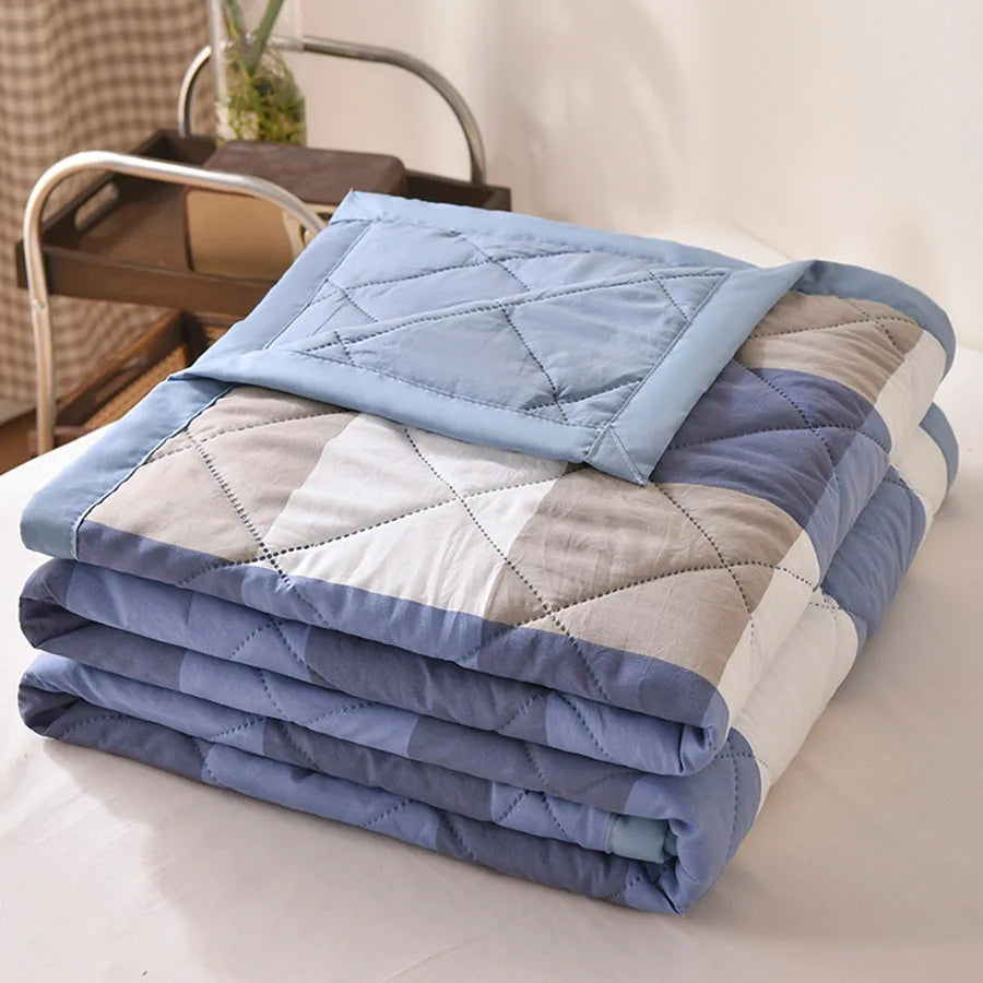 Blue, grey, and white block check quilted comforter with a light blue border, folded on a bed