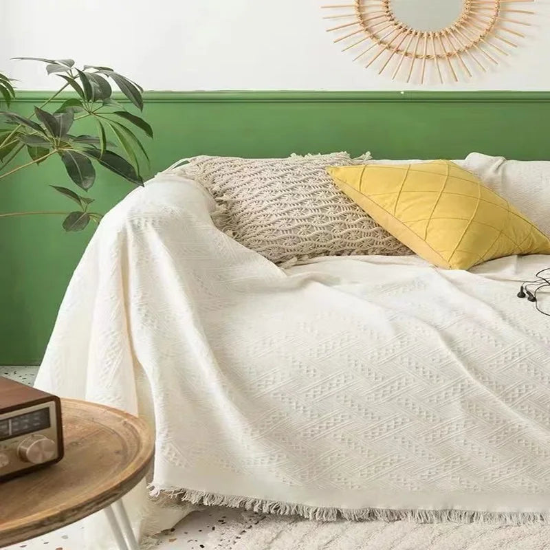 Bed with a soft cream blanket, a grey textured throw, and a yellow pillow against a green wall.