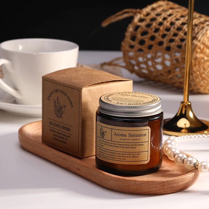 Candle jar with packaging on a wooden tray next to a cup and decorative items.