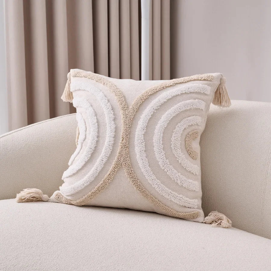 Decorative pillow with tassels on a beige sofa against a neutral background