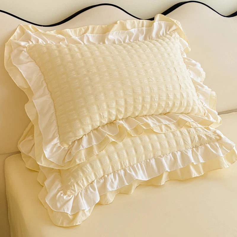 Cream-colored ruffled pillow on a matching blanket and bedspread.