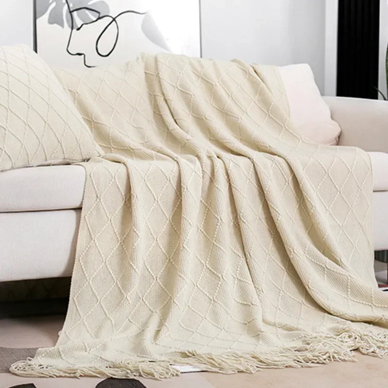 Cream diamond-patterned knit throw with tassel fringe draped across a sofa with a matching textured cushion