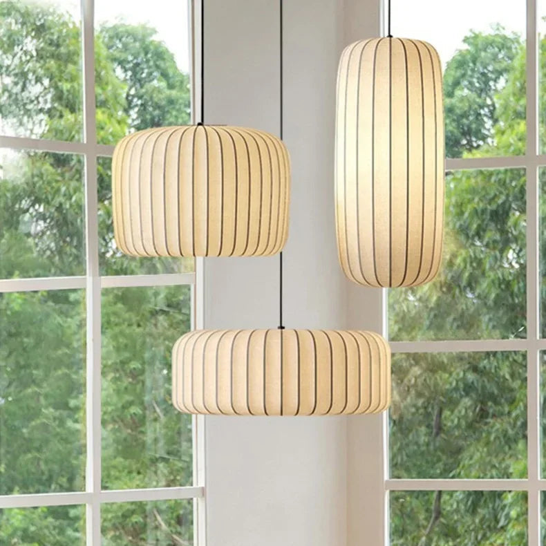 Three pendant lights hang in front of a window with greenery outside.