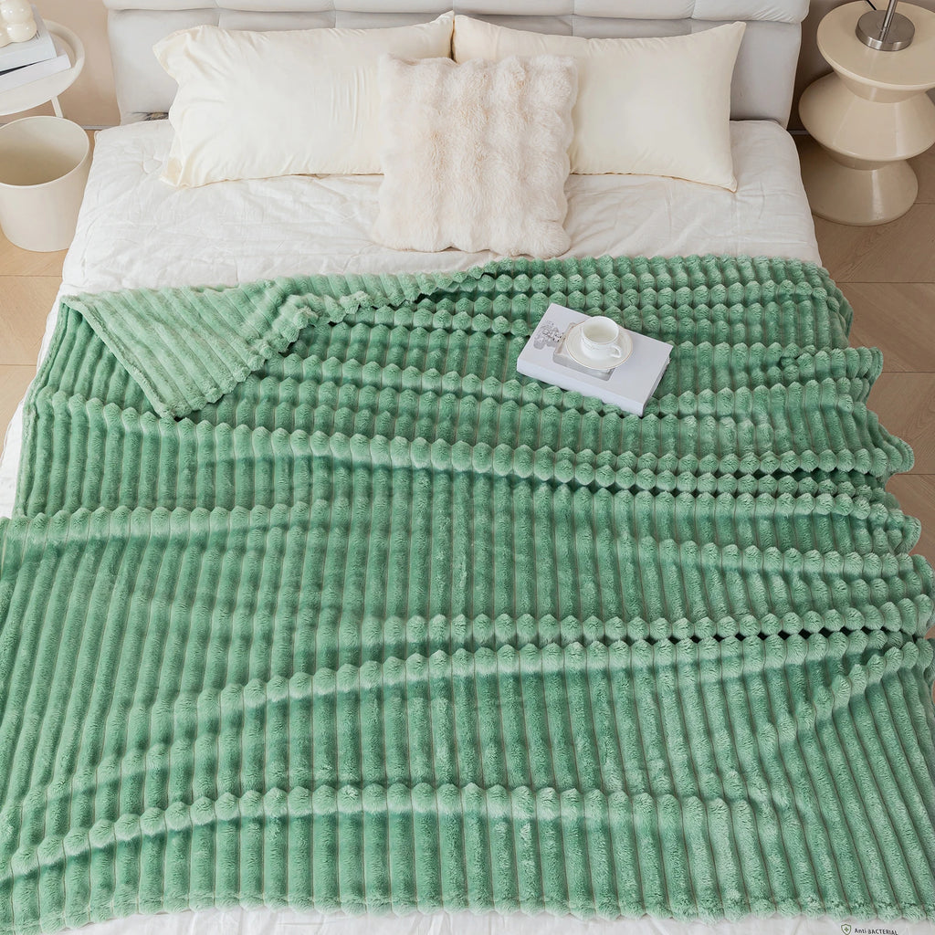 Green textured blanket draped over a bed with pillows and a small card on a wooden floor.