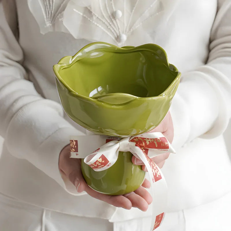 Person holding a green ceramic bowl with a white ribbon