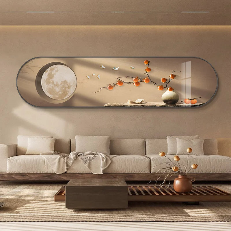 Modern horizontal oval wall light featuring a branch of persimmons and a full moon graphic, illuminated by a soft LED glow from behind the frame in a neutral-toned living room.