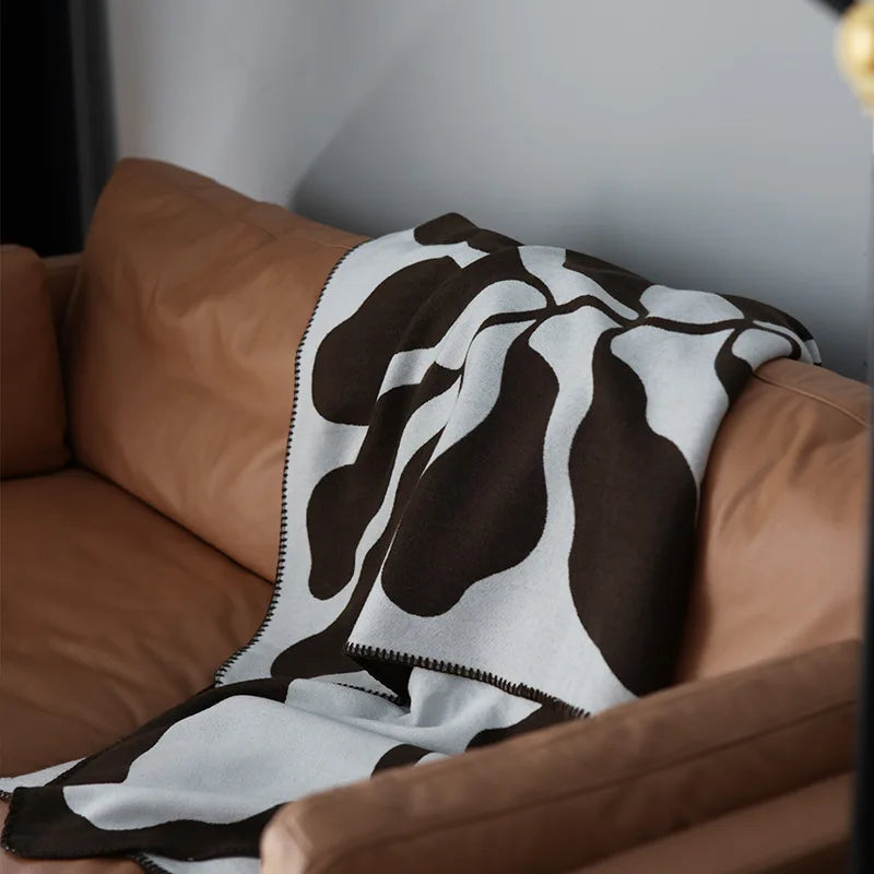 Mocha and grey abstract jacquard blanket draped over a wooden chair on a textured cream rug