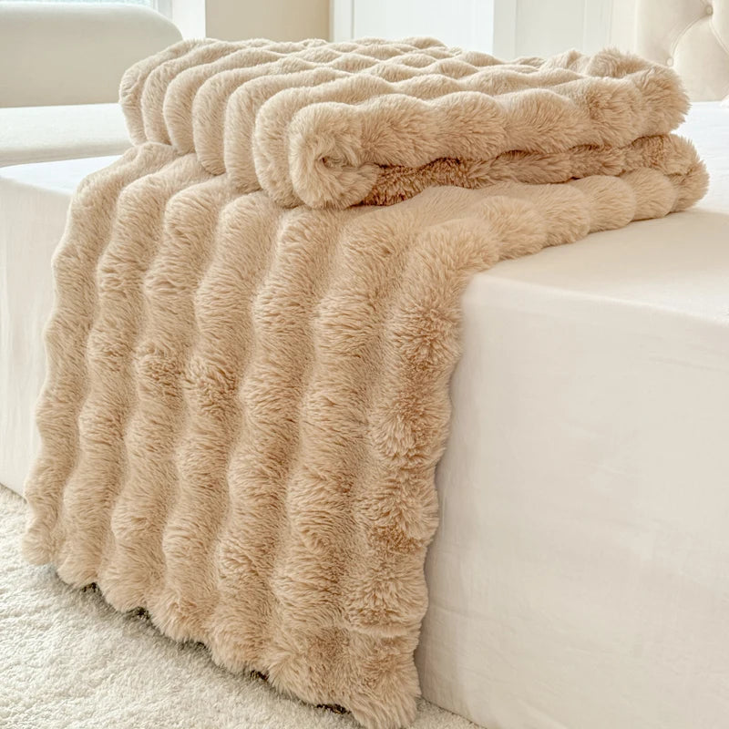 Beige fluffy blanket draped over a white sofa in a bright room.