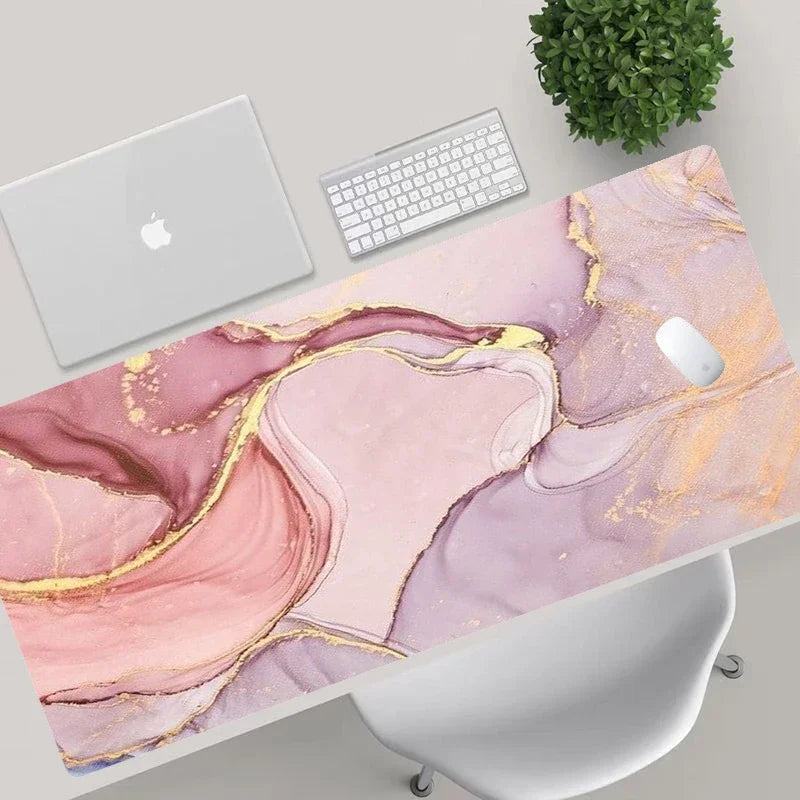 Desk setup with a pink and gold marble desk pad, laptop, keyboard, and mouse.
