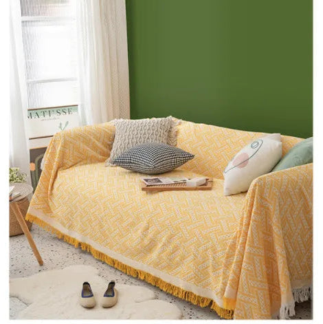Yellow blanket draped over a sofa with decorative pillows in a room with green walls and a window.