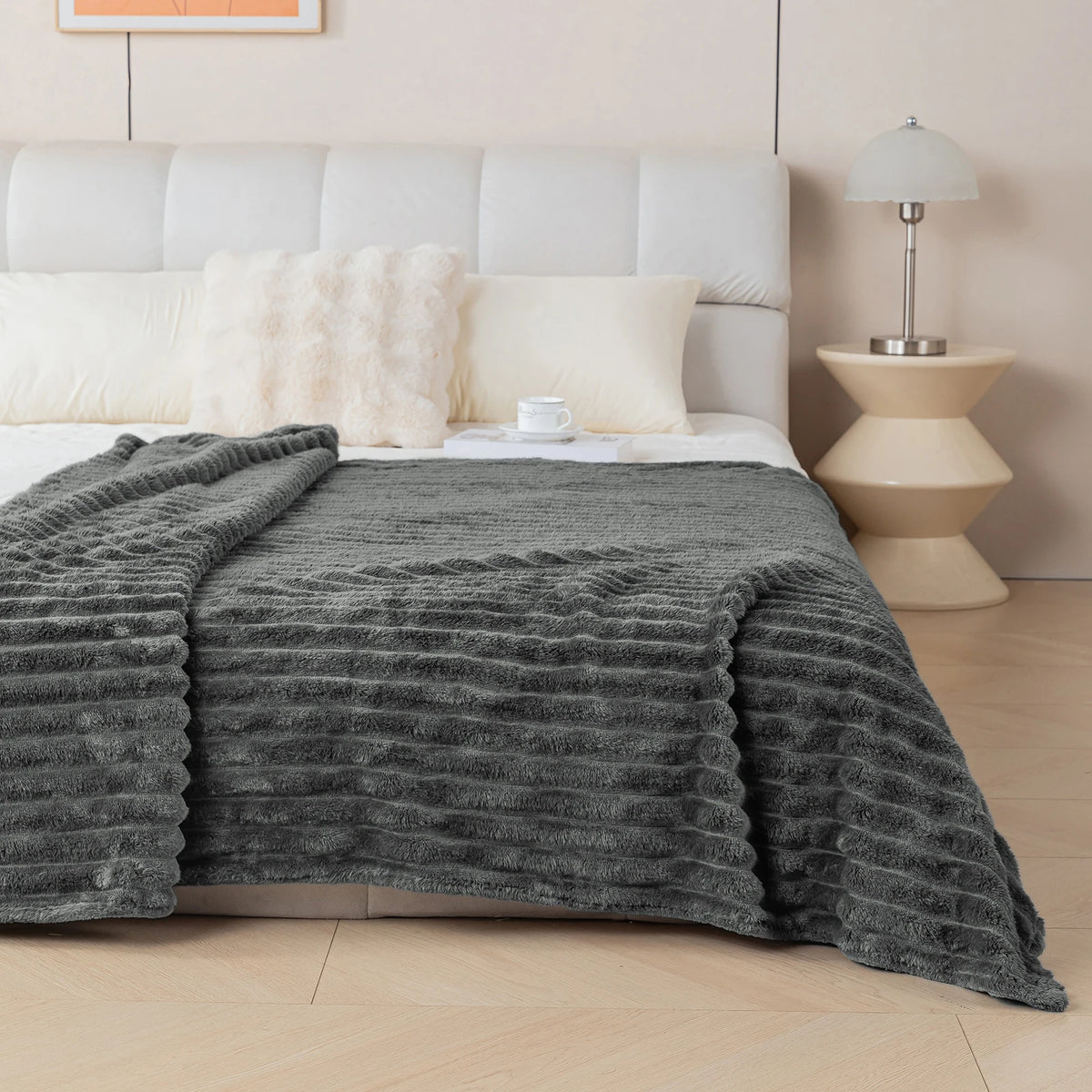 Charcoal-grey textured blanket on a bed in a bedroom setting, with a lamp and side table.