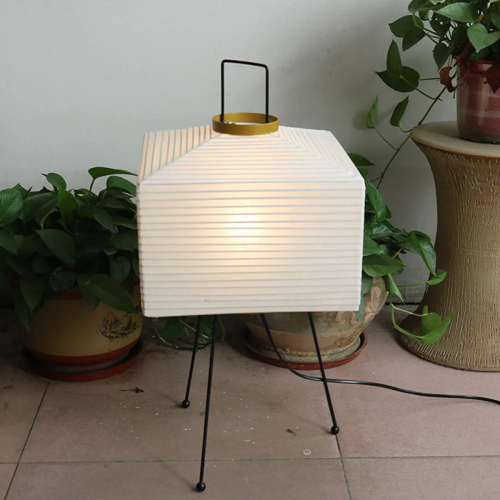 A Japanese floor lamp with a white woven lampshade and a black metal base in a room with plants.