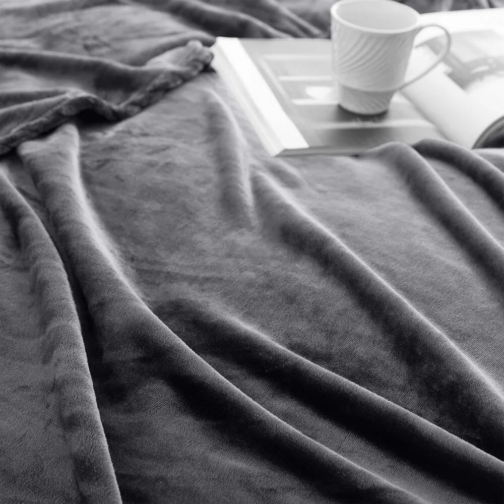 A close-up of a grey blanket draped over a surface with a white mug and book in the background.