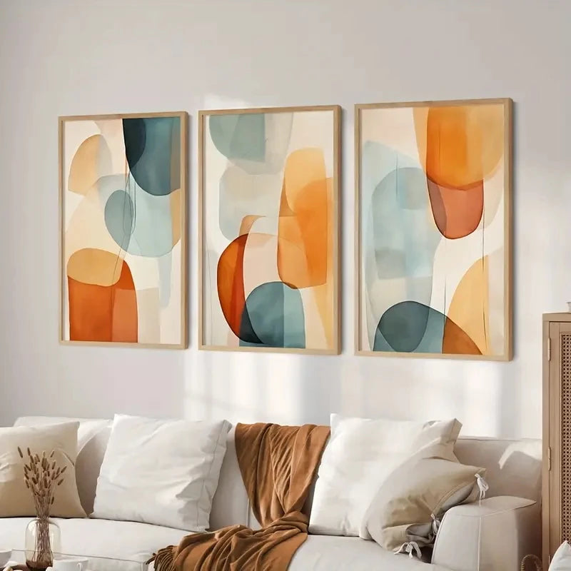 Three abstract art pieces hanging above a sofa with decorative pillows.
