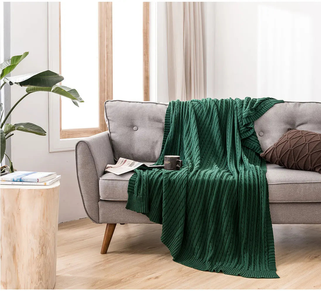 Green blanket draped over a grey sofa in a living room with a plant and coffee table.