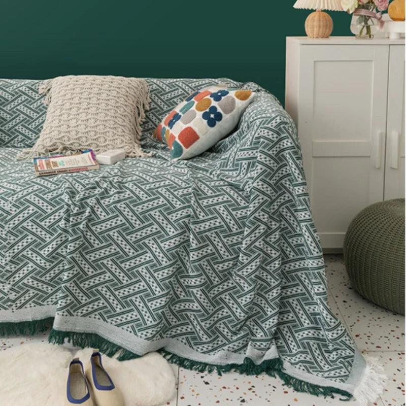 Patterned green blanket draped over a bed with pillows and a nightstand in the background.