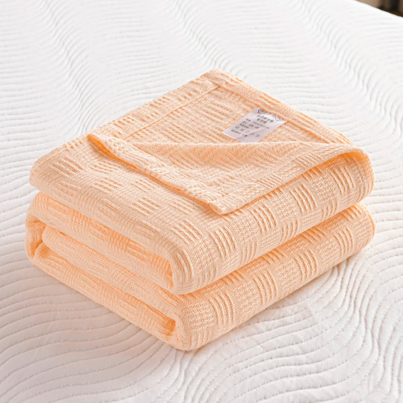 Folded cream cotton knit blanket with basket weave texture and care label on white bed