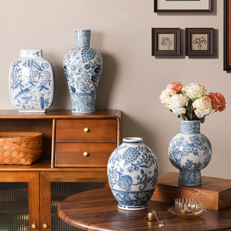 Decorative vases with floral patterns on a wooden cabinet and table against a wall with framed artwork.