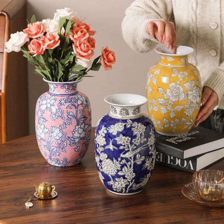 Three decorative vases on a wooden table with a person interacting with one of them.