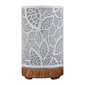 Minimalist leaf pattern essential oil diffuser with white metal sleeve and dark wood grain base.