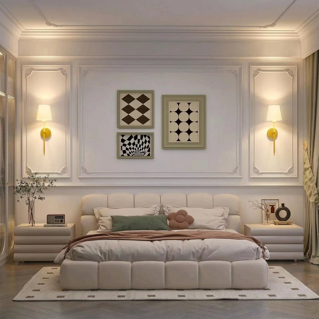 Pair of gold wall sconces with white shades mounted on either side of a bed.