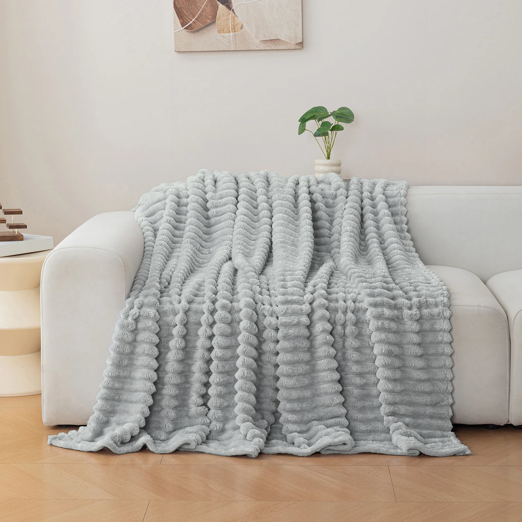 Light grey textured blanket draped over a white sofa in a living room setting.