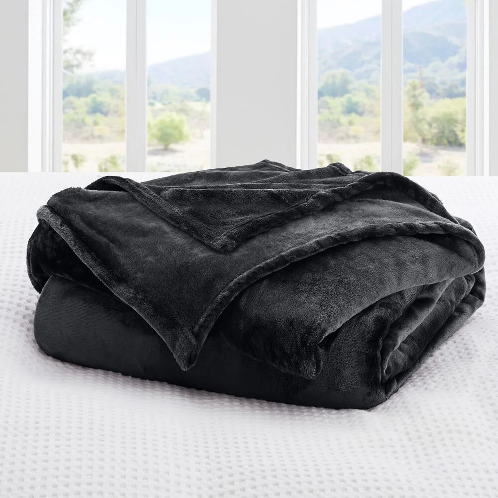 A charcoal black plush blanket on a bed with a window view of trees and mountains.