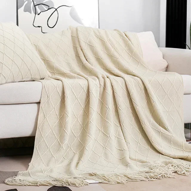 Cream diamond-patterned knit throw with tassel fringe draped across a sofa with a matching textured cushion