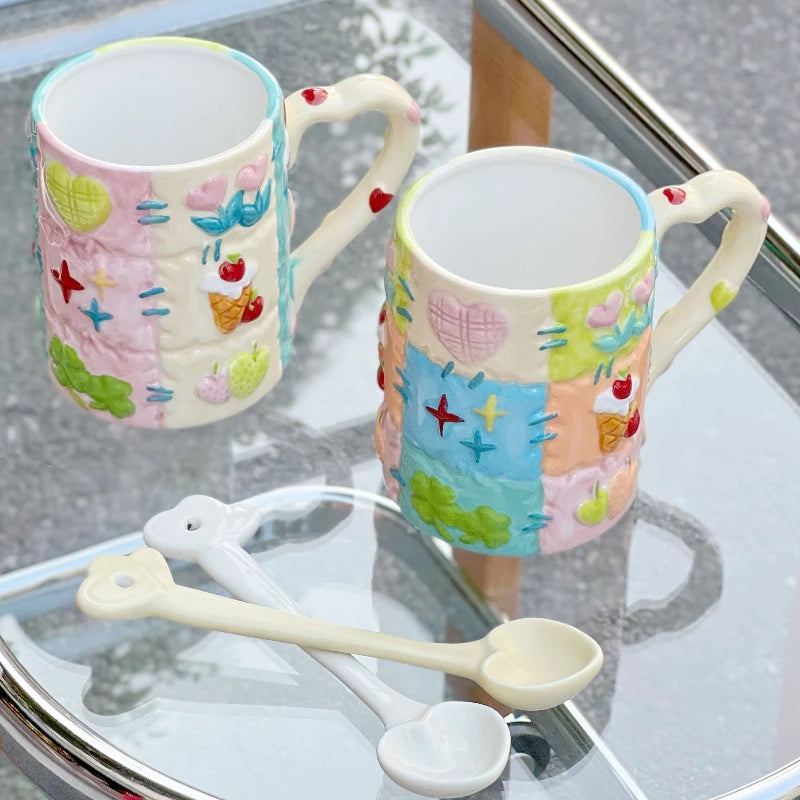 Two colorful ceramic mugs with decorative patterns on a glass surface, accompanied by a small white spoon.