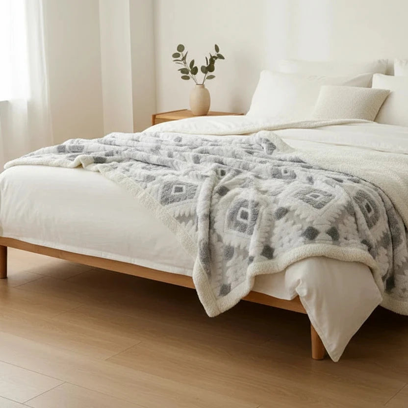 Bed with a patterned gray throw blanket in a bedroom setting.