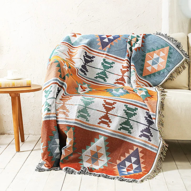 Earth-toned woven throw with sage green and terracotta geometric designs and fringed edges.