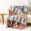 Earth-toned woven throw with sage green and terracotta geometric designs and fringed edges.