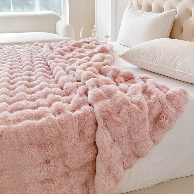 Pink fluffy blanket on a bed with white pillows and a neutral-colored room.
