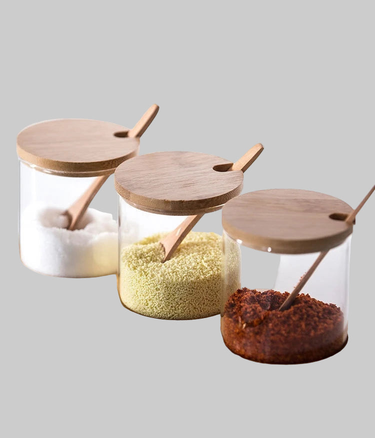 Three glass containers with wooden lids on a tray, containing different spices and seasonings.