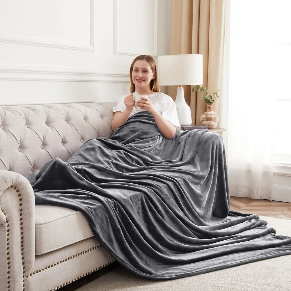 A woman sitting on a couch with a stone grey blanket draped over her, holding a mug.
