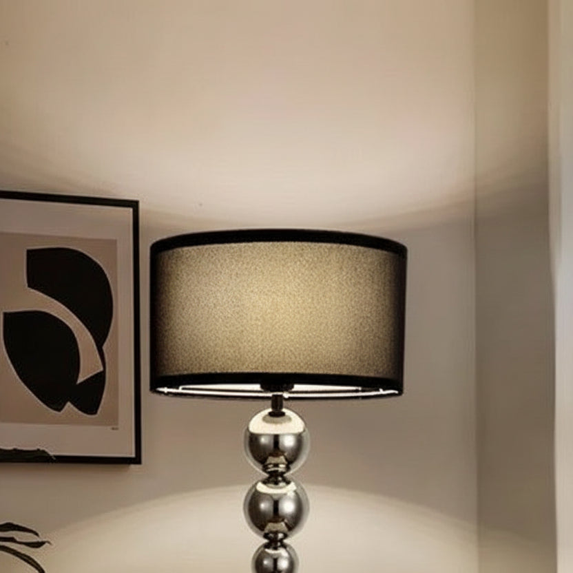 A floor lamp with a black shade and a silver base on a neutral background