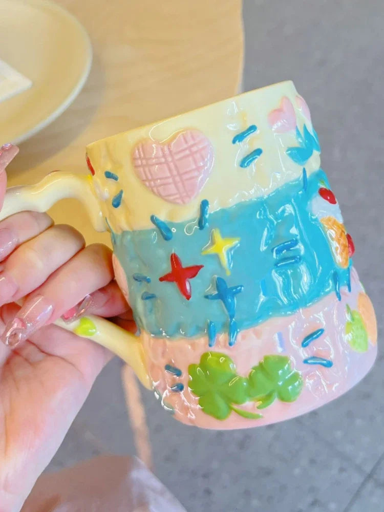 Colorful mug with starfish, hearts, and other designs held by a hand.