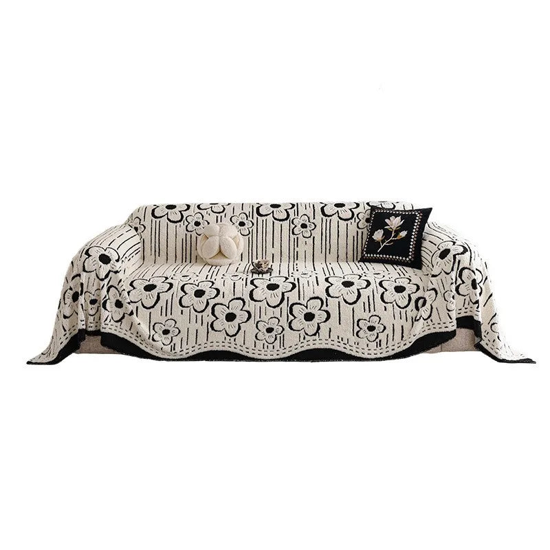 Cream and black floral-patterned sofa throw with bold contrast edging, neatly layered over a modern armchair sofa in a bright interior setting.