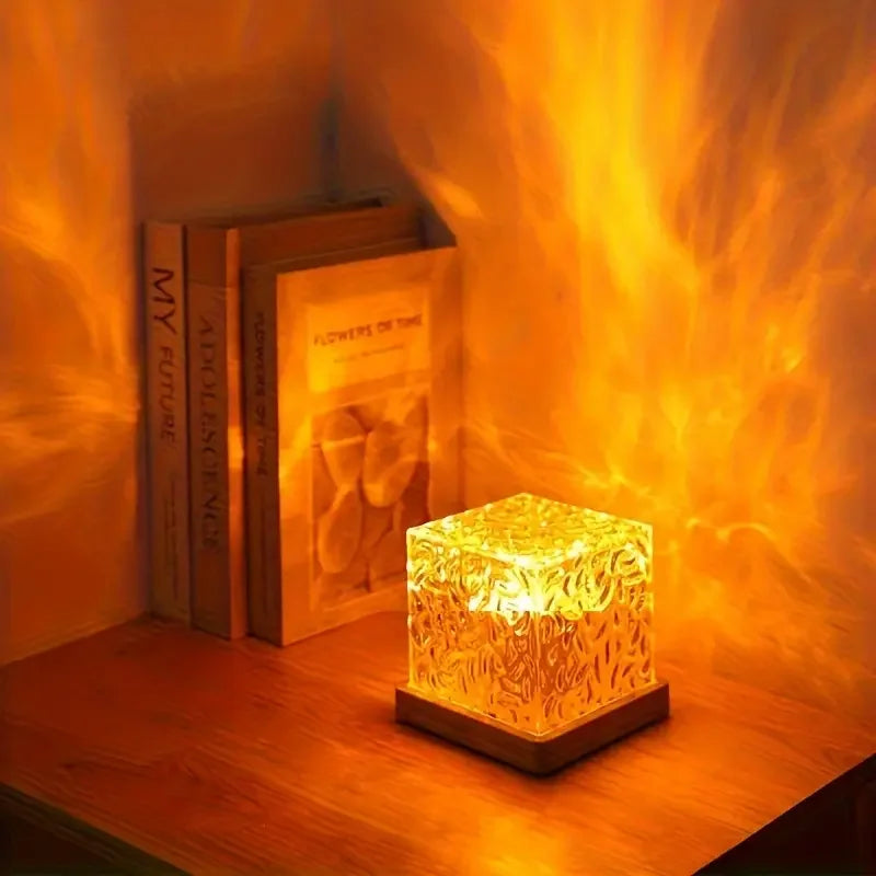 Decorative cube lamp emitting a warm glow on a wooden surface with books in the background.