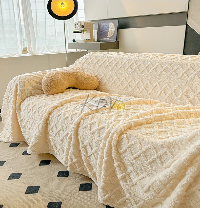 Beige textured blanket draped over a sofa in a room with a lamp and decor items.