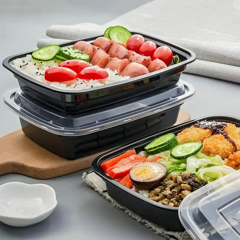 Three black meal prep containers with various food items on a light gray surface.