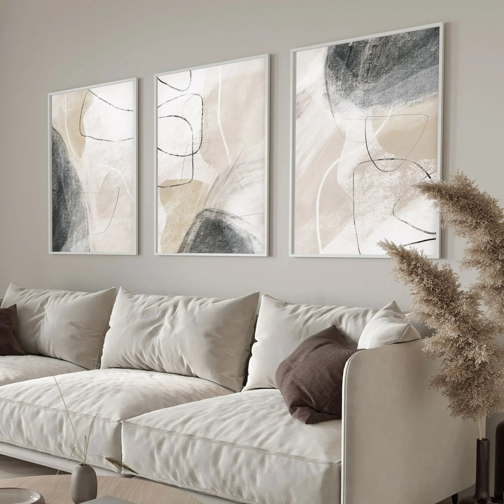 A set of three charcoal and beige minimalist prints in white frames above a plush white sofa.