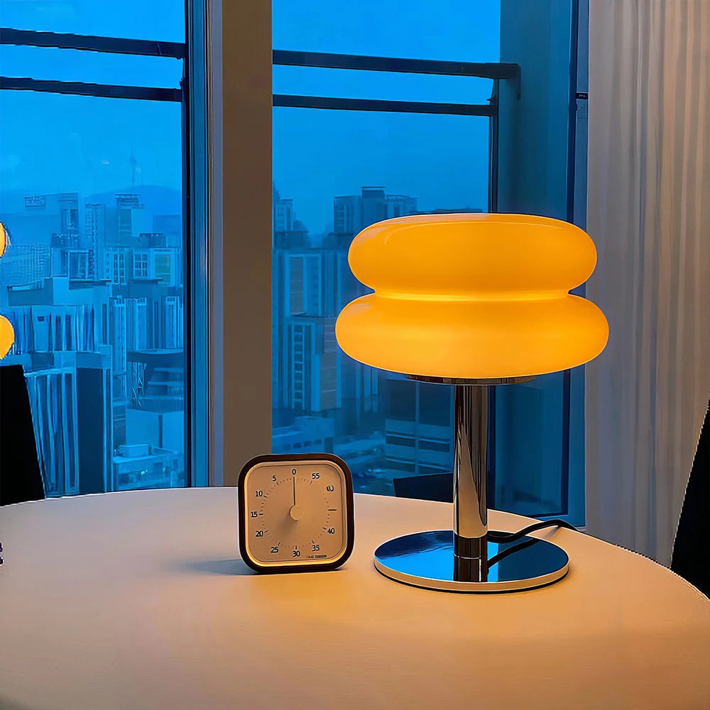 An orange glowing modern light in a room with large windows showing a cityscape.