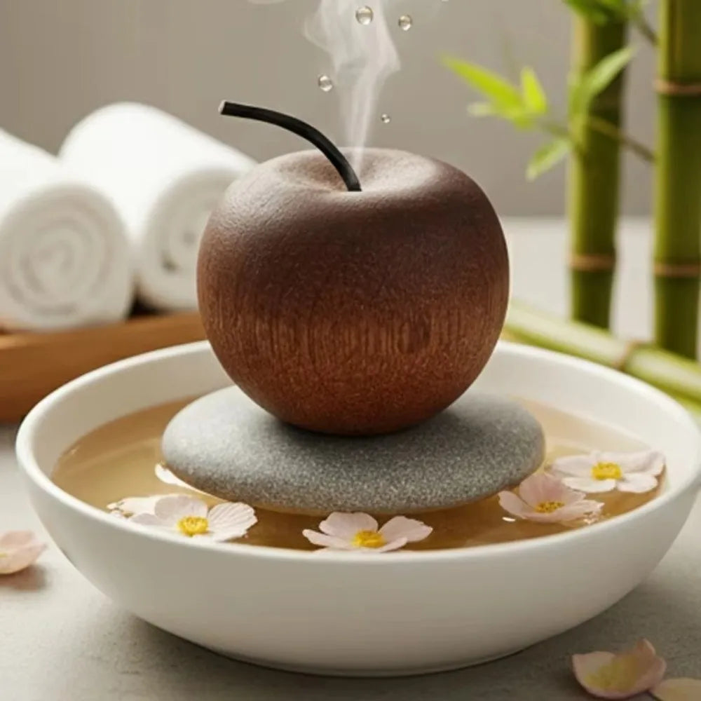  Apple-shaped diffuser with steam rising, placed on a stone in a bowl of water with flowers.