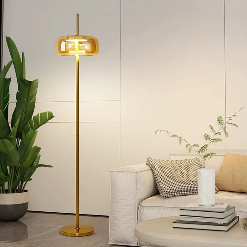 Minimalist gold floor lamp with amber glass shade lit in a warm glow.