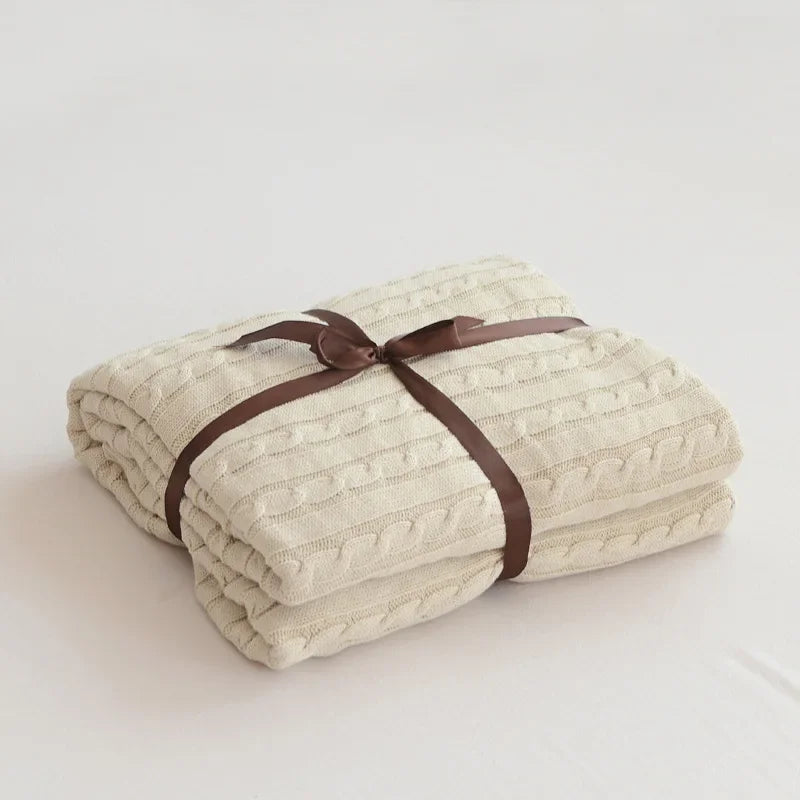 Folded beige blanket tied with a brown ribbon on a light background