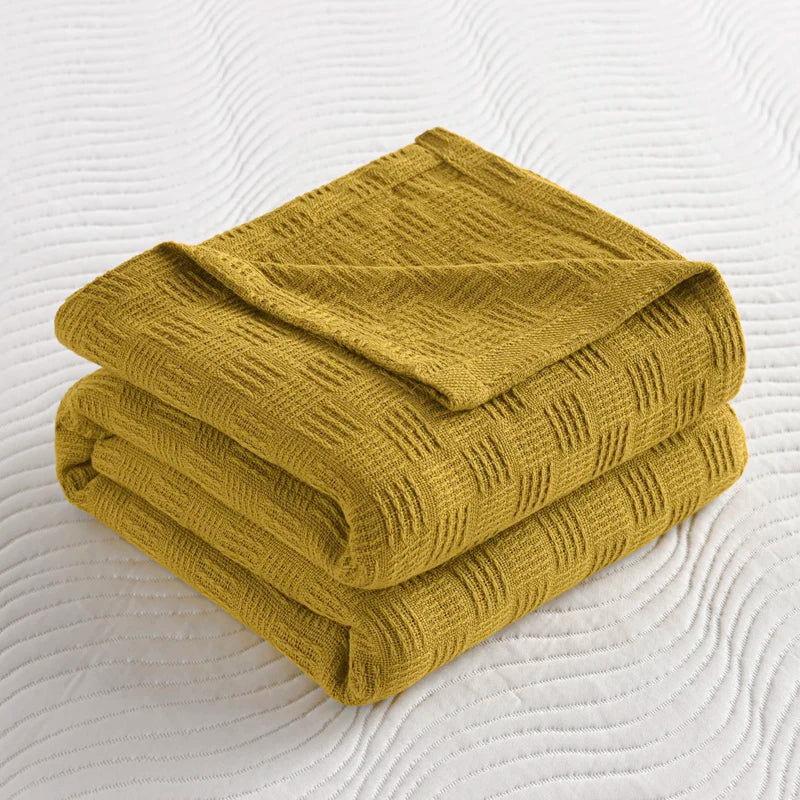 Folded olive cotton knit throw blanket with textured weave pattern on white bedding