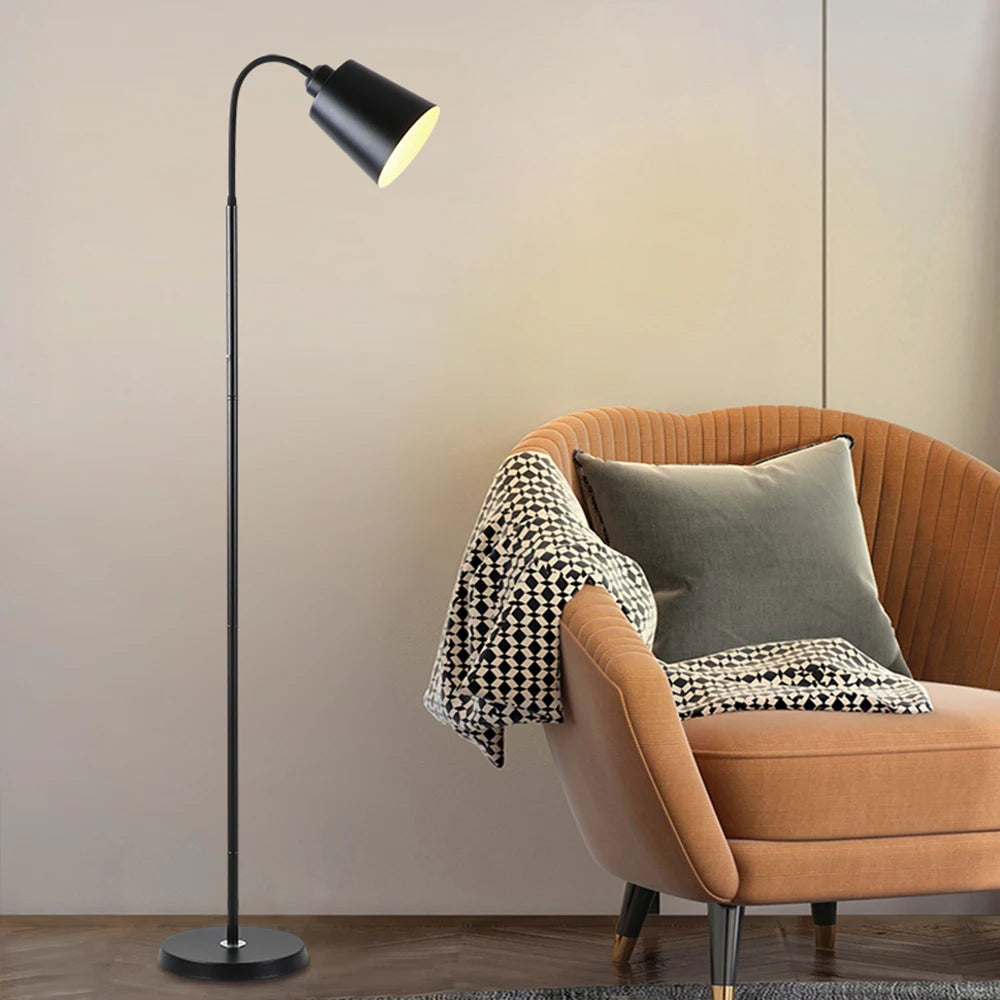 Modern black floor lamp next to a brown armchair with cushions and a blanket.